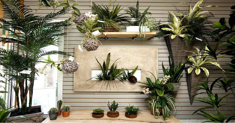 Artificial plants and trees arranged in a room, on shelves, a wall panel and a table